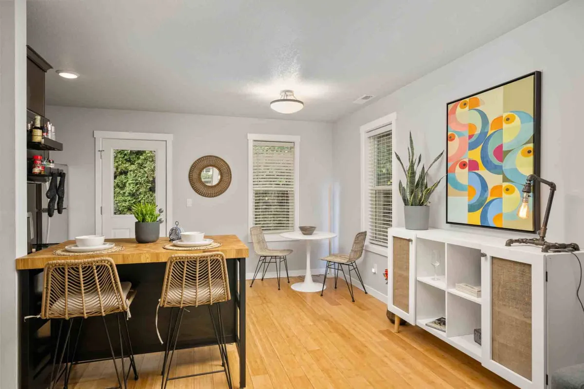 A cozy dining area centered around a round table, framed by colorful wall art and a kitchen island with bar stools in the background. The setting evokes warmth and encourages casual dining, entertaining, and intimate conversation.