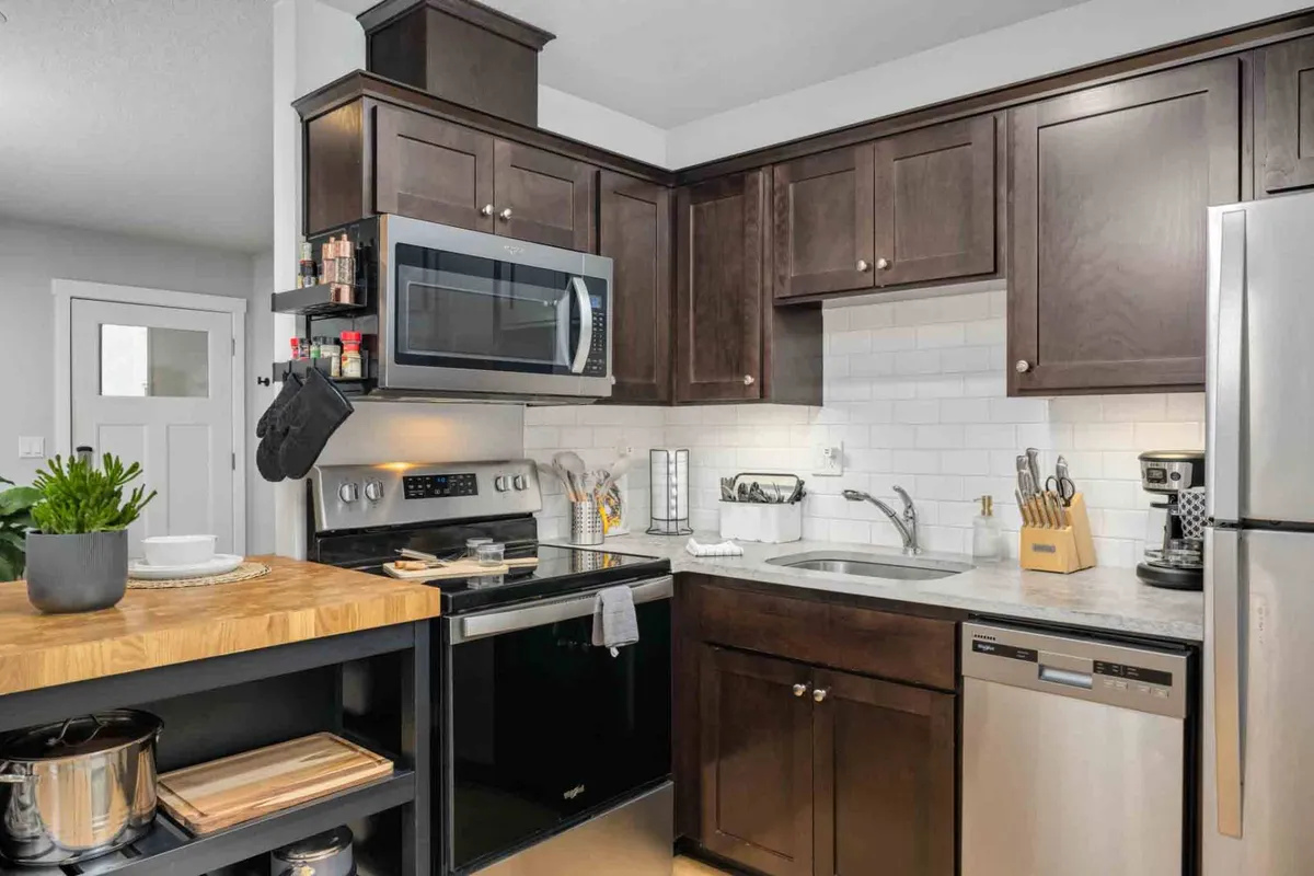 A bright, inviting kitchen with a wood-topped island, dark modern cabinetry, and stainless steel appliances. The layout encourages family cooking and casual meals together, with plenty of space for parents and children to gather.