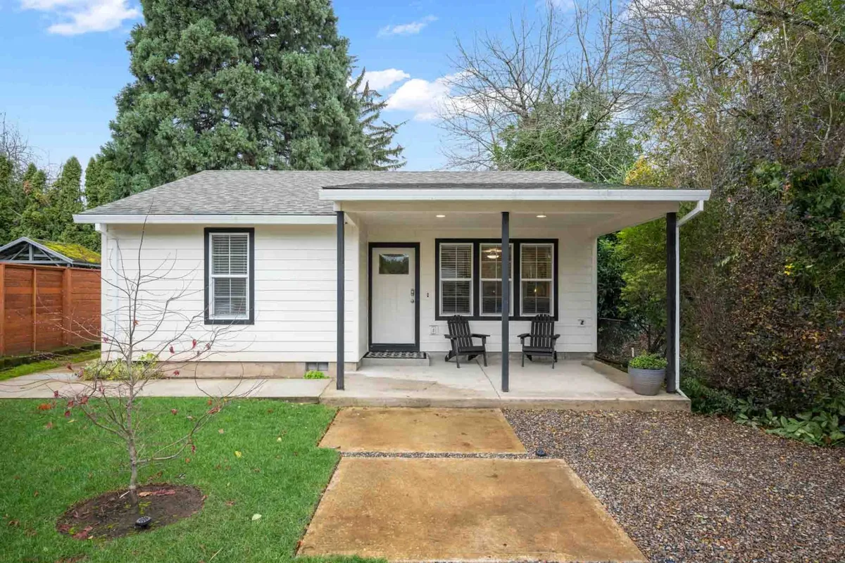 The image depicts a charming front porch set in a peaceful residential area, featuring two inviting black chairs surrounded by greenery and a well-kept pathway. The cozy setup suggests a welcoming spot for morning coffee or relaxing in the fresh air, emphasizing the tranquil ambiance of the outdoor space.