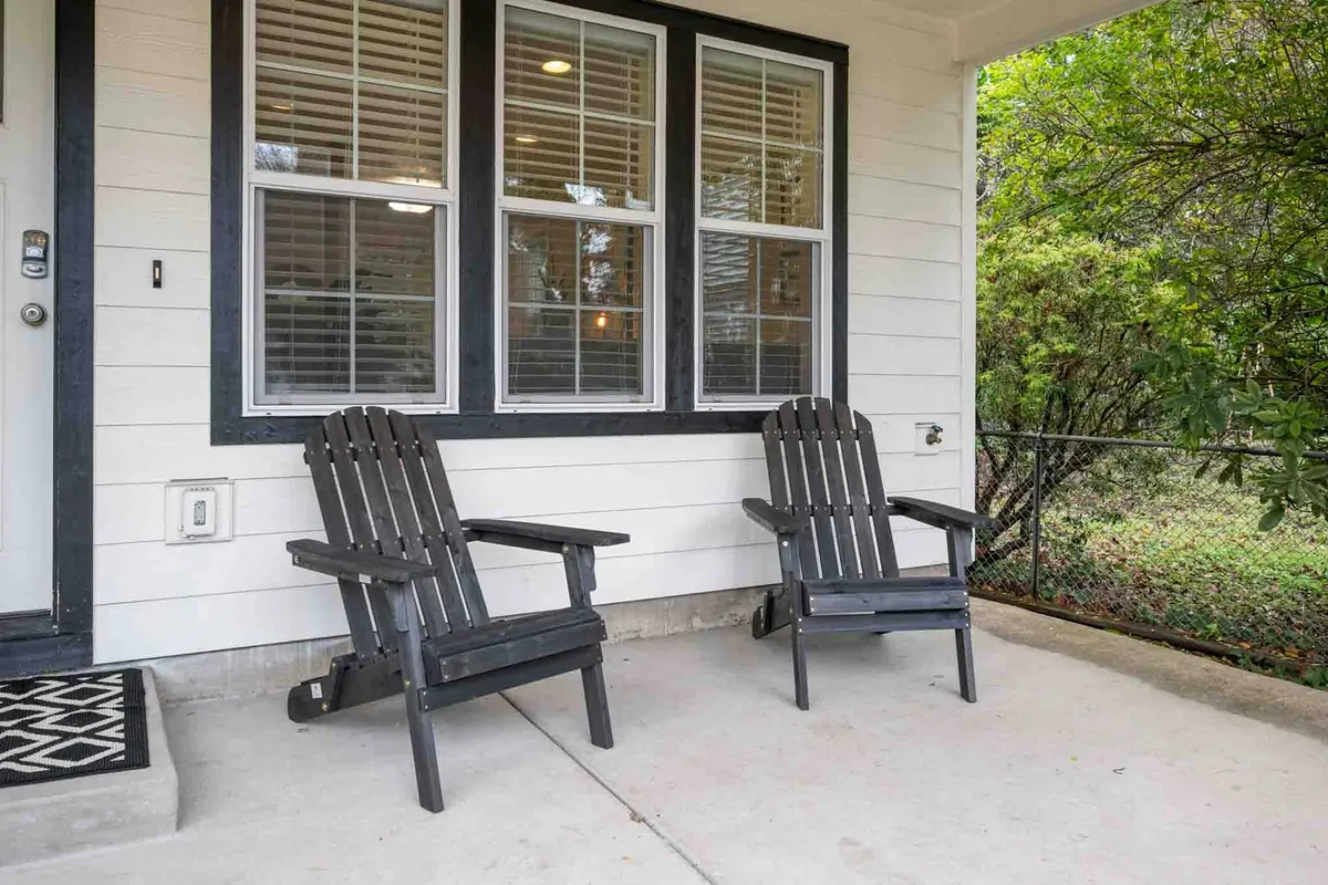 This exterior image features two black Adirondack chairs situated near large windows and the front door, suggesting a seamless flow between indoor comforts and outdoor serenity. The mood is calm, welcoming, and perfect for socializing or enjoying a peaceful moment in the breeze.
