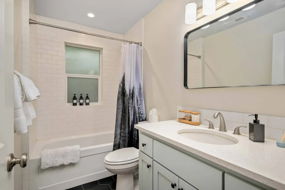 A sparkling, modern bathroom featuring a vanity with a clean sink, a large mirror, and a shower curtain with a soothing forest design. The space feels fresh, bright, and inviting—perfect for energizing morning routines or relaxing evening rituals.